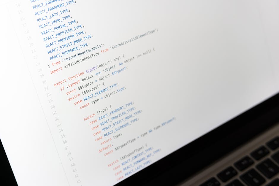 A close-up view of a computer screen displaying lines of JavaScript code in various colors, including blue, red, and black, with a portion of a keyboard visible at the bottom right. The code appears t