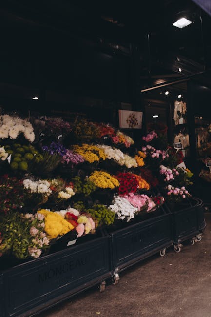 An indoor display of an extensive variety of fresh flowers arranged in black metal carts at Mayfairflowers.co.uk. The floral displays feature a vibrant mix of colours, including bright yellow chrysant