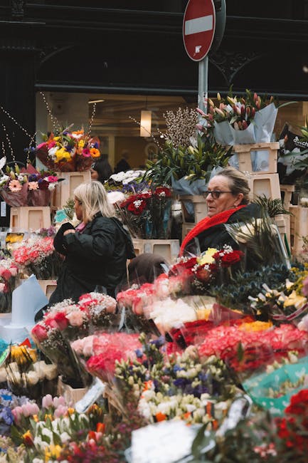 A bustling flower market with a variety of fresh floral arrangements and bouquets, featuring vibrant colours such as reds, pinks, yellows, and whites. Numerous flower bouquets wrapped in light blue ti