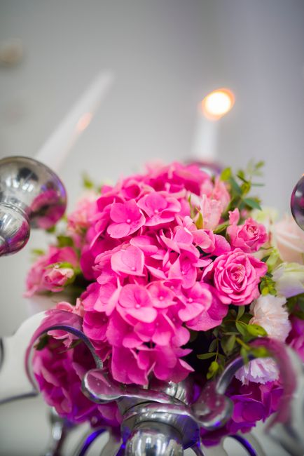 A vibrant floral arrangement featuring bright pink hydrangeas and small pink roses, with green foliage accents, arranged in a compact bouquet. The flowers have fresh, delicate petals and sturdy stems,