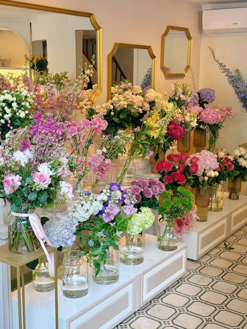An interior display of multiple floral arrangements featuring a variety of fresh flowers such as pink and purple hydrangeas, white roses, yellow and pink blossoms, and lush greenery, arranged in clear