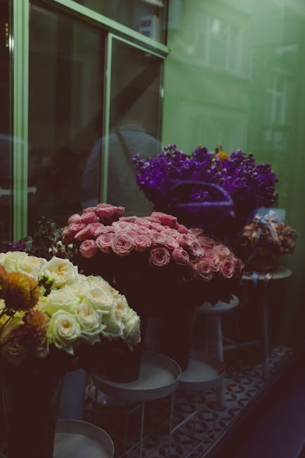 A display of fresh floral arrangements inside a flower shop window, featuring a variety of bouquets with vibrant colors. The arrangement in the foreground showcases soft pink roses with delicate petal