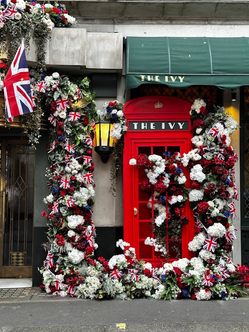 A vibrant floral display decorating the exterior of The Ivy restaurant, featuring a red British phone box adorned with white, red, and navy blue flowers including hydrangeas and carnations, intertwine